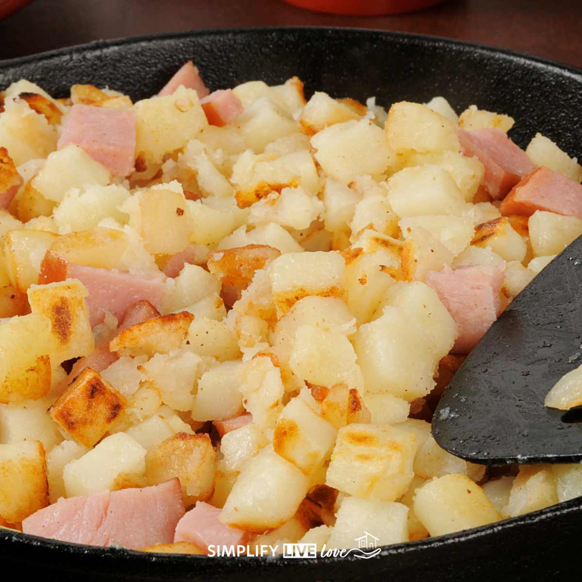 fried potatoes and ham in cast iron skillet with black spatula