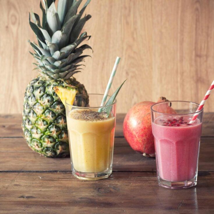 pineapple and pomegranate smoothies on brown counter with pineapple and pomegranate in background