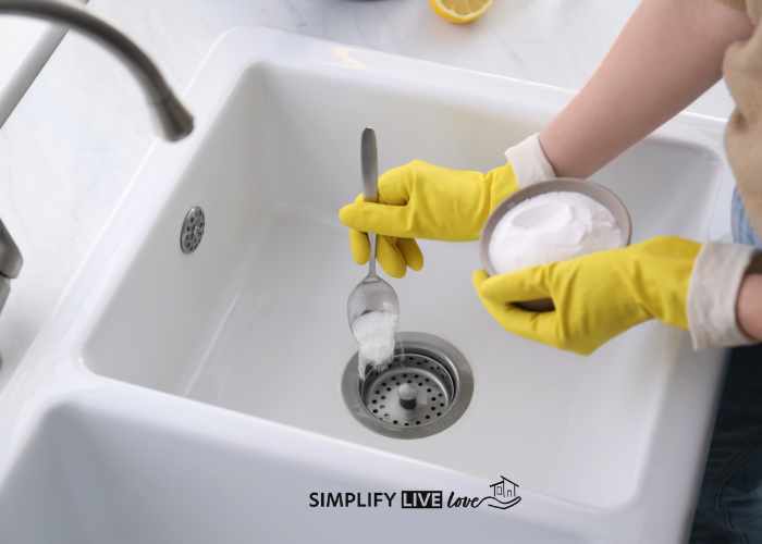 woman wearing yellow gloves using baking soda to deodorize drain in kitchen sink