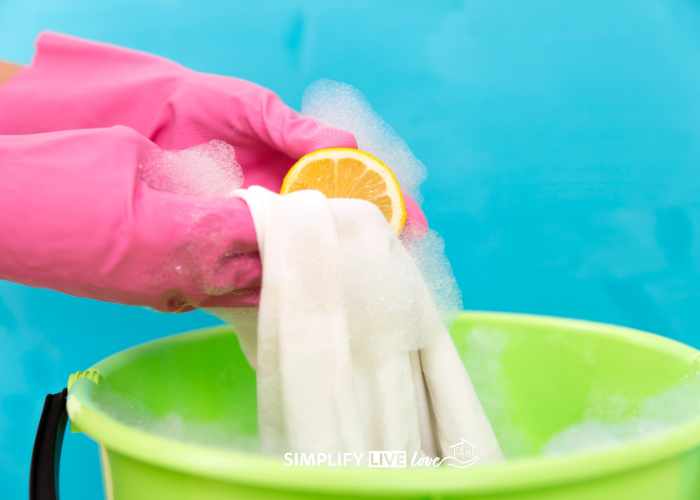 hands in pink gloves using lemon to remove stain from white clothing in steaming green bucket of water
