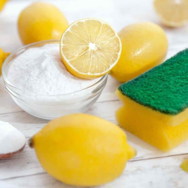 natural cleaning products lemons, baking soda, and sponge on white wooden countertop