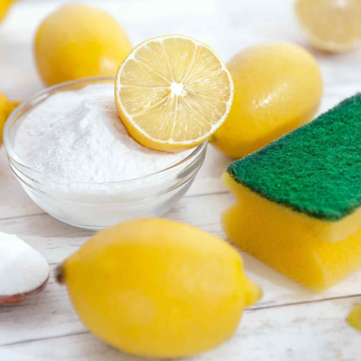 natural cleaning products lemons, baking soda, and sponge on white wooden countertop
