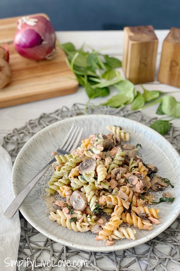 delicious salmon pasta on a white plate with onions and spinach leaves in background