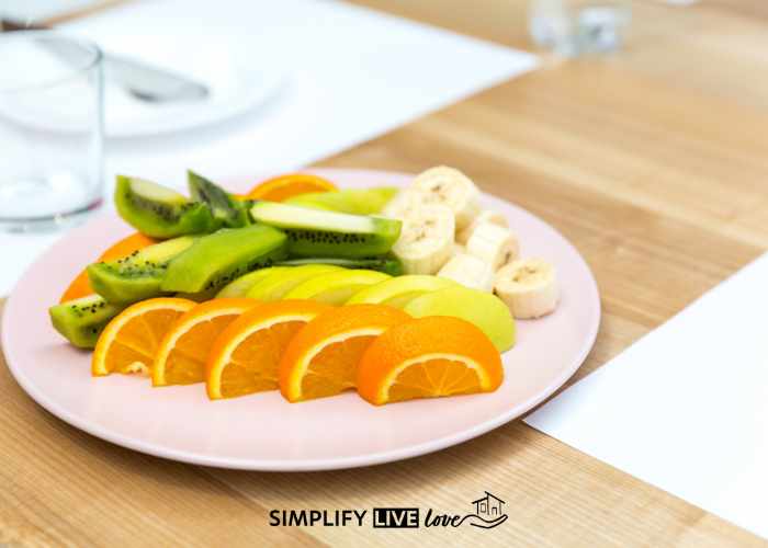 sliced kiwi, orange, banana, and lemon on a plate with glass of water beside it