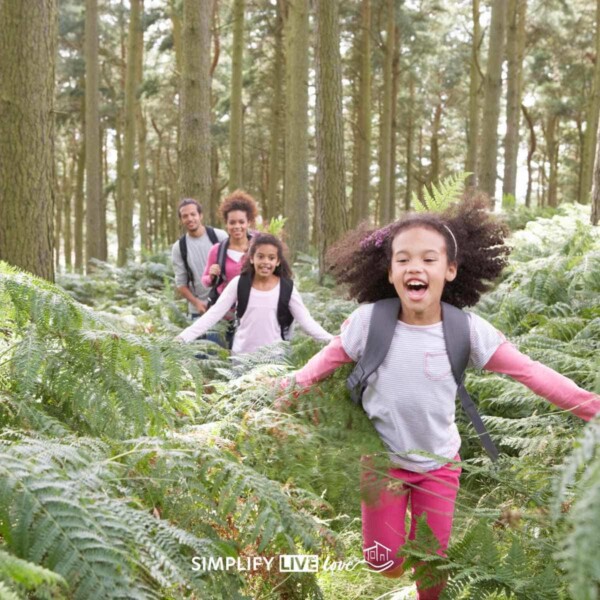 girl with brown curly hair running through forest ferns with borther and parents in the background