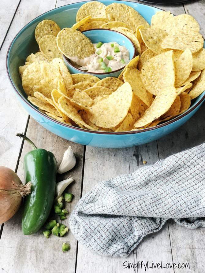 tortilla chips in blue platter with jalapeno popper dip in the central well. jalapenos and a kitchen towel lay on the table beside the platter