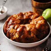 caramel apple monkey bread in white bowl with apples in background