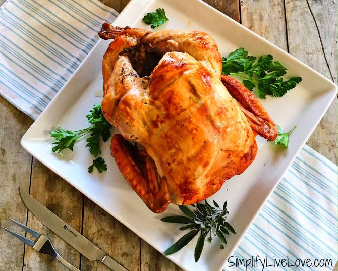 Upside down roasted turkey in a white platter with green garnish and herbs.  Striped towel on wooden counter underneath the platter