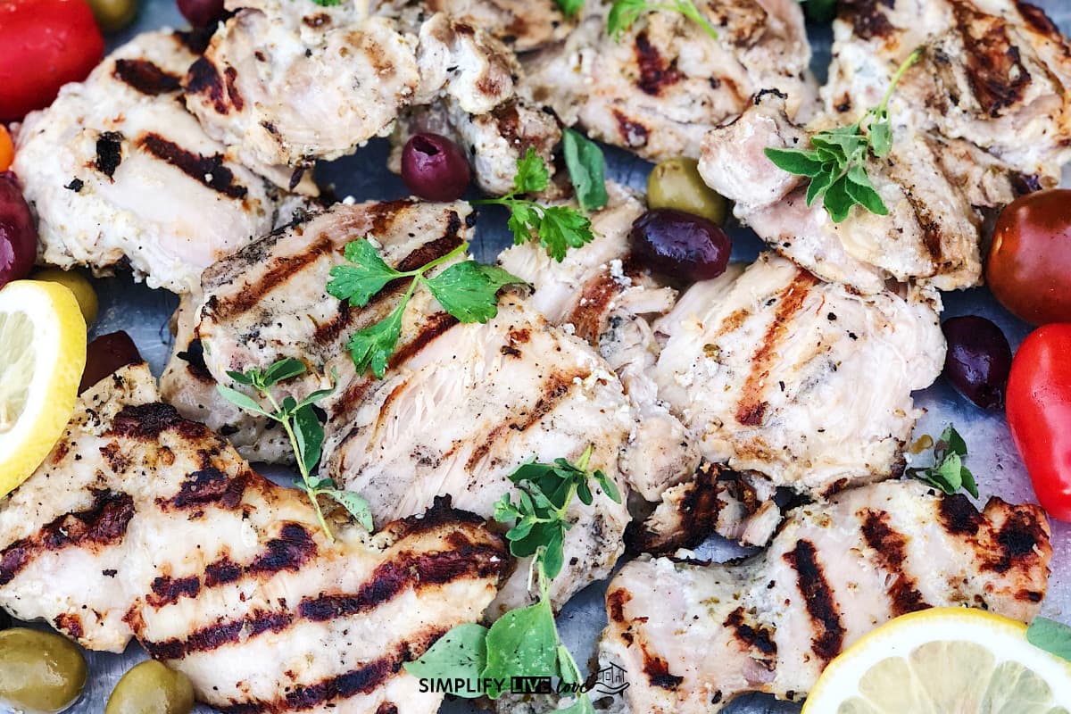 greek chicken breasts plated with olives, lemon, and tomatoes