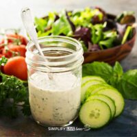 jar of healthy greek yogurt ranch dressing in front of cucumbers, tomatoes, and salad bowl