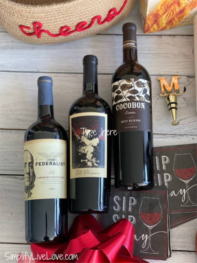 three bottles of wine with a gold wine stopper and cocktail napkins for wine and cheese baskets