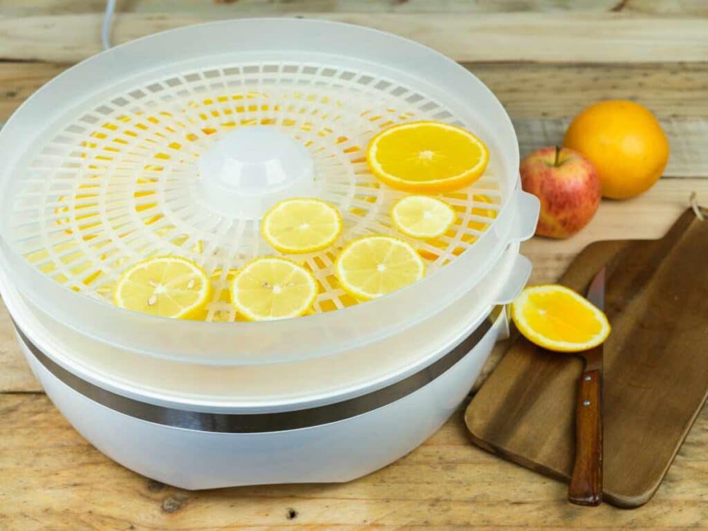 orange slices in food dehydrator trays on wooden countertop