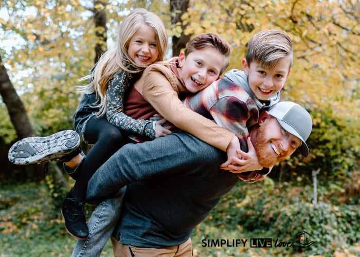 man hiking with three kids in the woods giving them a piggy back ride