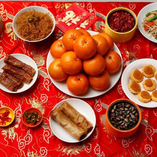 good luck food for Chinese New Year with oranges, spring rolls, and other foods on red and gold tablecloth