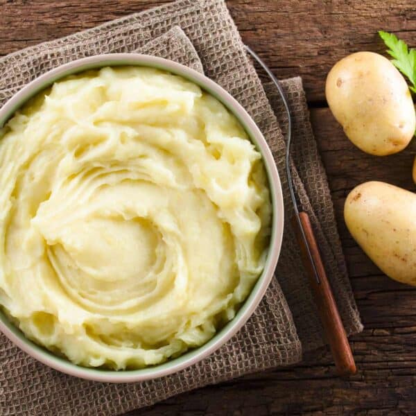 instant pot mashed potatoes in bowl with raw potatoes laying next to it on table