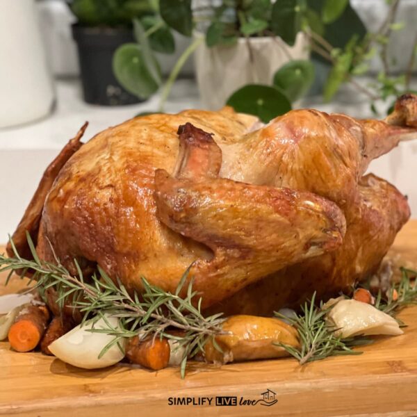 Upside down roasted turkey with golden brown skin on a wooden cutting board with fresh rosemary, roasted carrots, and onions