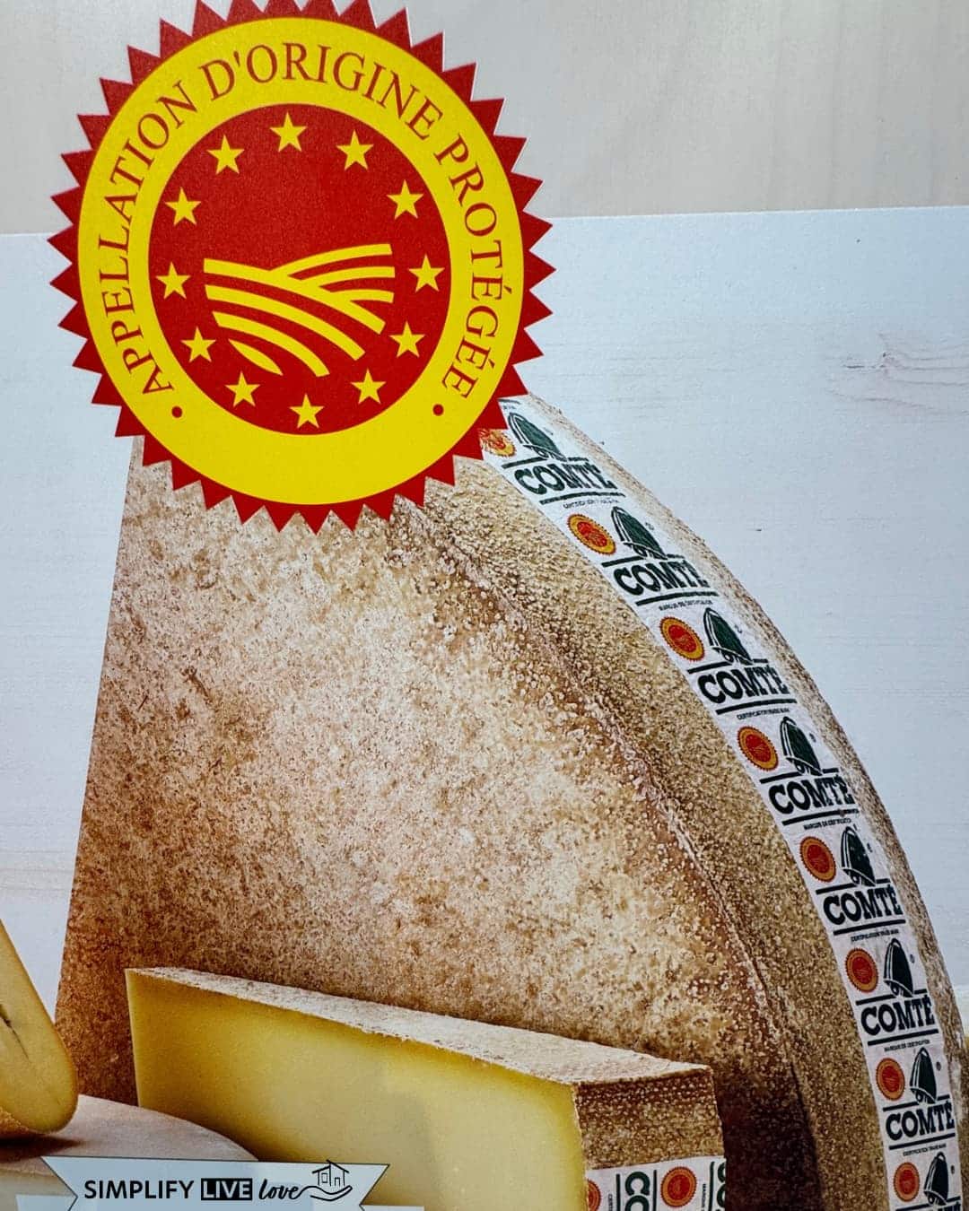 Display at the Maison du Comté showing the red and yellow Appellation d’Origine Protégée seal beside a wedge of Comté.