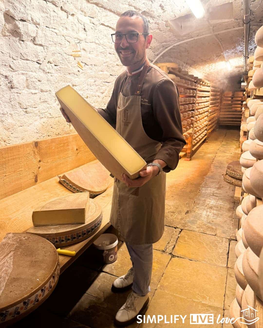 Marc Janin holding a slab of Comté in the cheese cellar of his cheese shop.