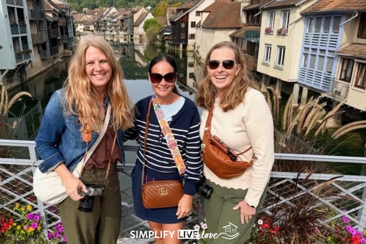 3 woman standing on a bridge with the village and the river in the background
